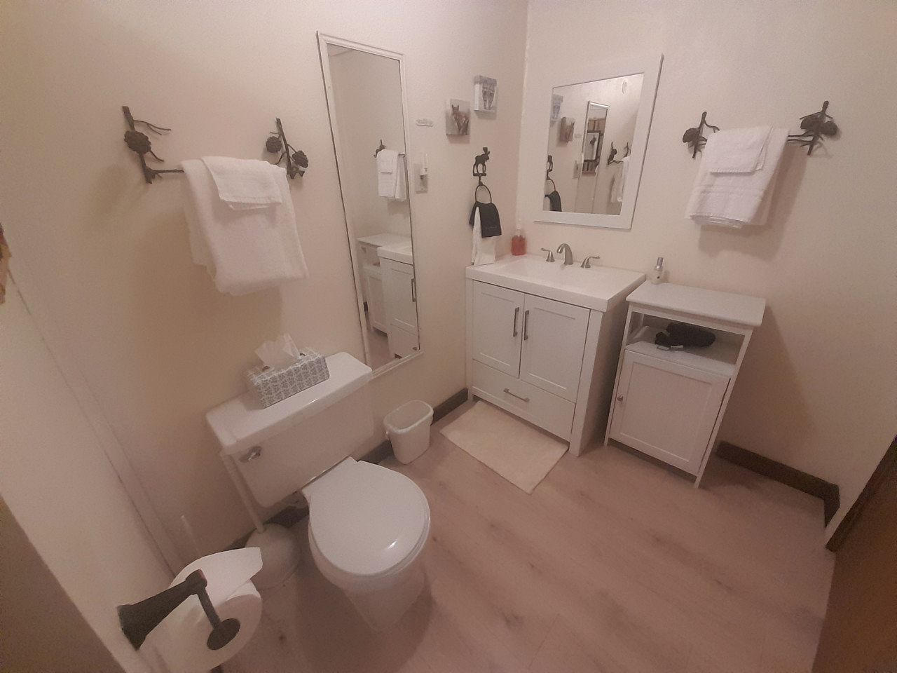 Un baño con inodoro, lavamanos, espejo y perchero para toallas.