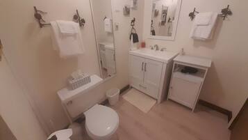 Un baño con inodoro, lavamanos, espejo y perchero para toallas.