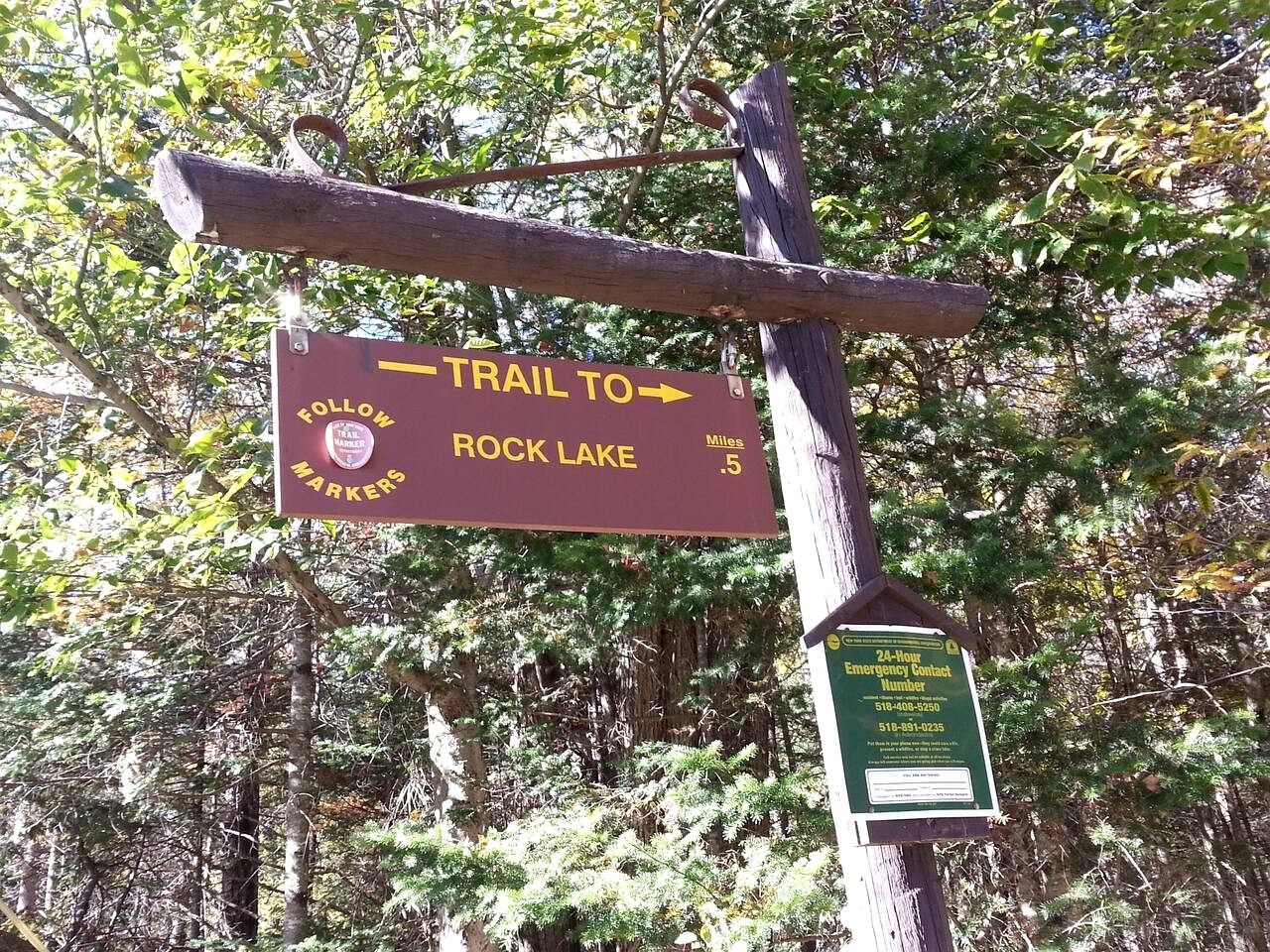 A trail sign pointing to Rock Lake, a 5-mile marker, and an emergency contact number.
