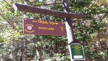 A trail sign pointing to Rock Lake, a 5-mile marker, and an emergency contact number.