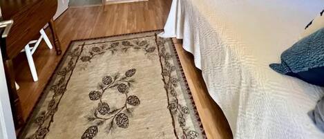 Un dormitorio con cama, escritorio, silla, alfombra y un baño visible a través de una puerta abierta.