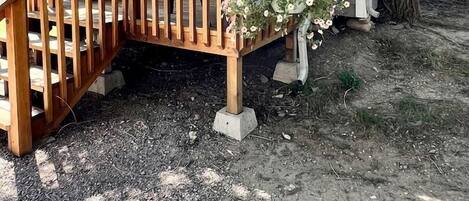 Una terraza de madera con barandilla, un porche cubierto y un pequeño jardín con flores.