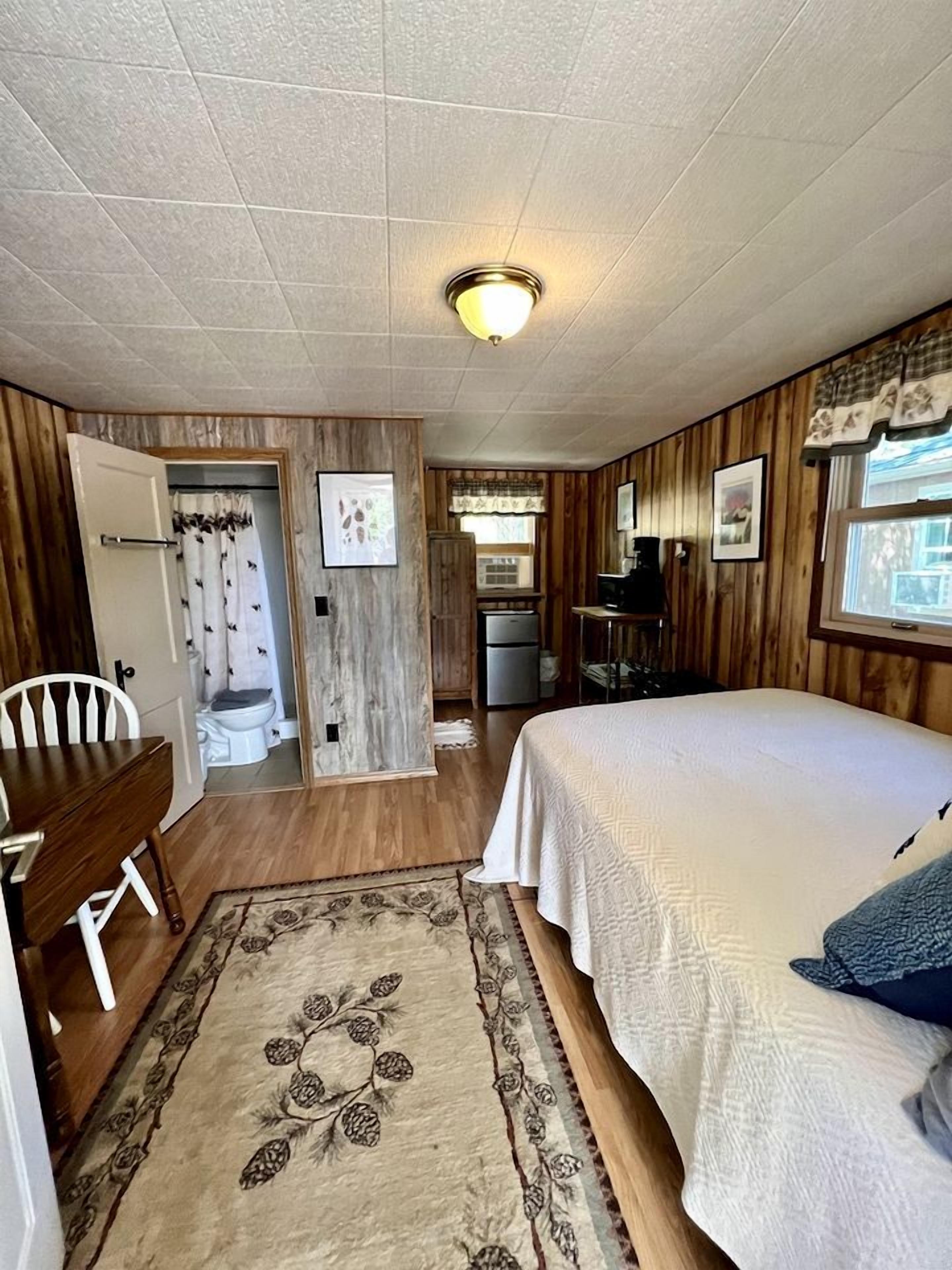 A room with a bed, a desk, a chair, a small kitchenette, and a bathroom.