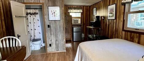 A room with a bed, a desk, a chair, a small kitchenette, and a bathroom.