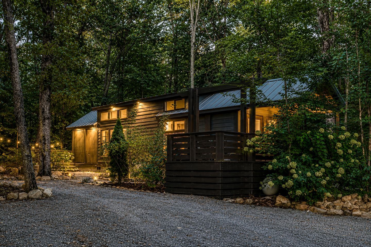 Une cabane en bois avec une allée en gravier, entourée d’arbres et d’une clôture en bois.