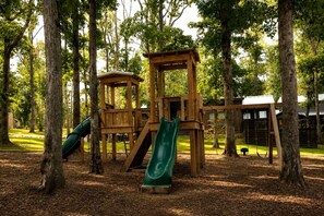 Un’area giochi in legno con scivoli e altalene, situata in un parco boschivo.