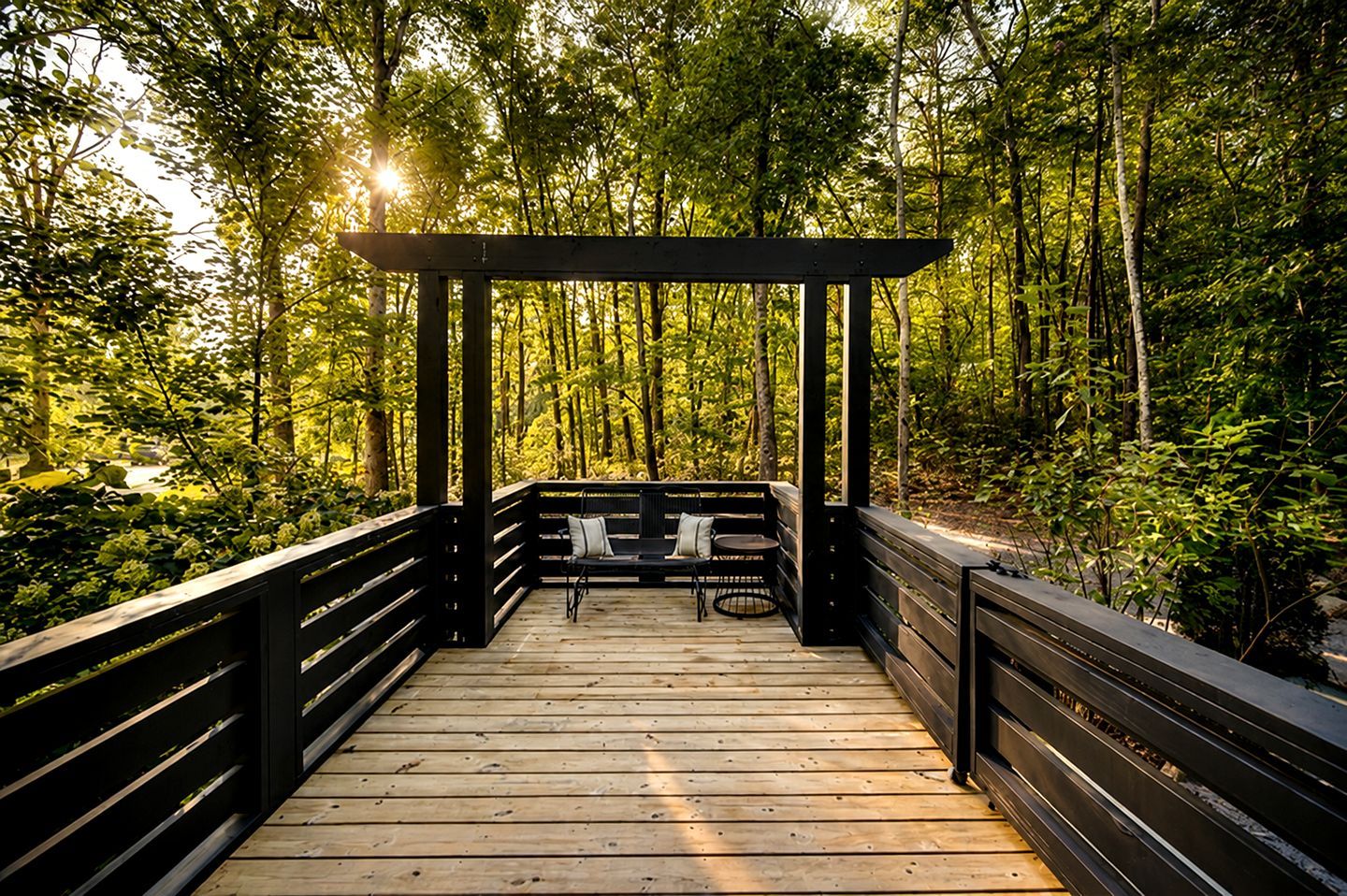 Una terraza de madera con una estructura de pérgola, rodeada de un bosque denso.