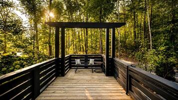 Una terraza de madera con una estructura de pérgola, rodeada de un bosque denso.