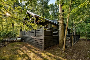 Eine Holzhütte mit geneigtem Dach, umgeben von dichten Bäumen und einem Holzzaun.