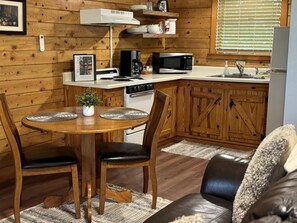 Una cocina acogedora de estilo rústico con paredes de madera, una mesa de comedor con sillas, un refrigerador, un microondas, una estufa y una cafetera.