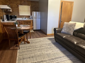 Un espacio habitable compacto con kitchenette, una zona de comedor con mesa y sillas, y un sofá con cojín decorativo.