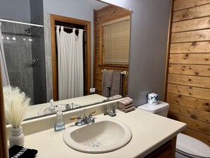 Une salle de bain équipée d’un lavabo, d’un miroir, d’une douche et de toilettes.