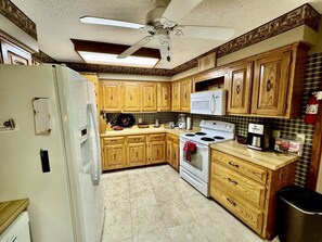 Una cocina con armarios de madera, un refrigerador blanco, una estufa y un ventilador de techo.