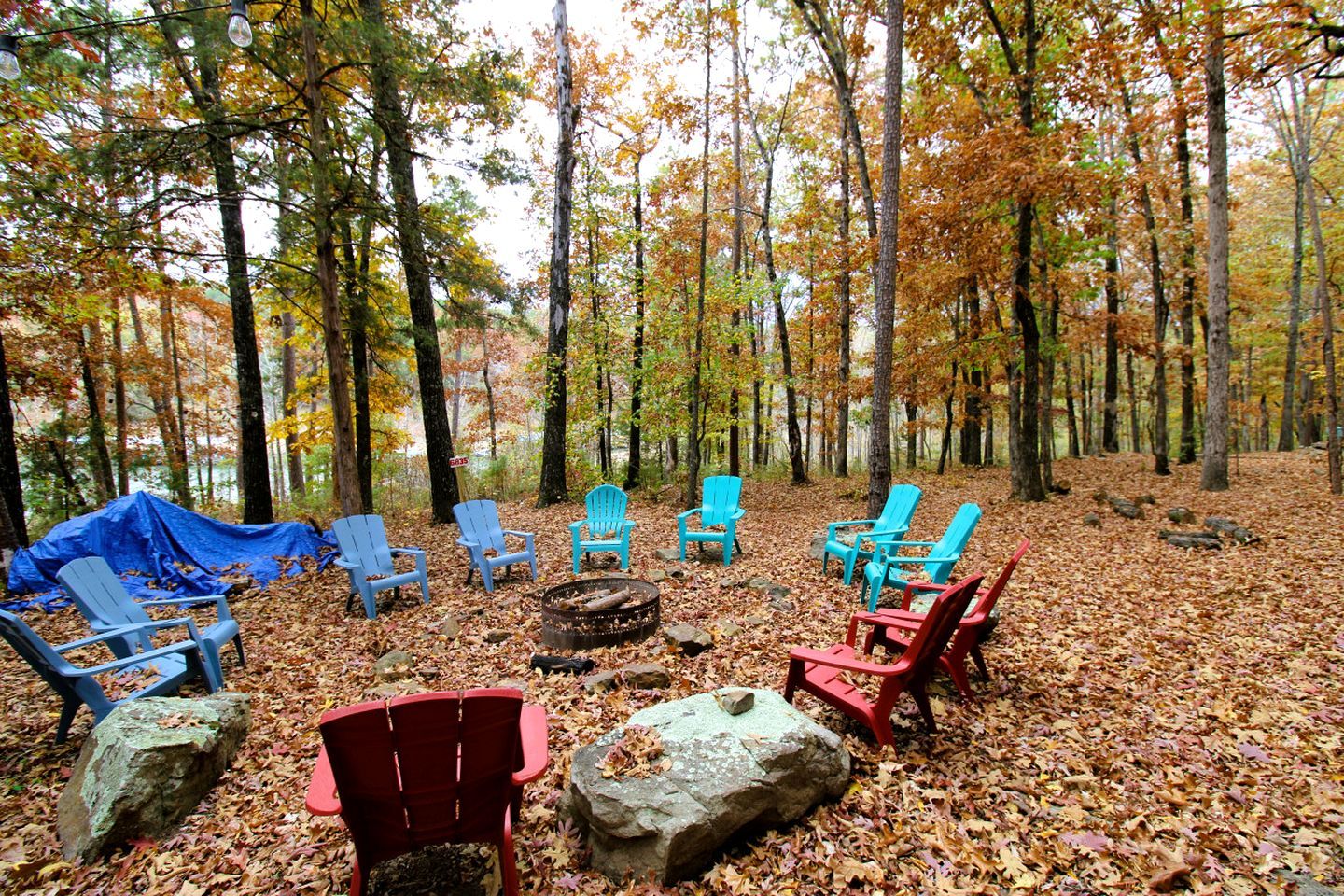 Un terrain de camping situé dans une forêt, avec plusieurs chaises Adirondack disposées autour d’un foyer central.