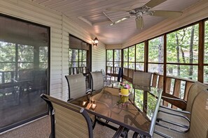 Un espace extérieur abrité, aménagé pour les repas, avec une table en verre, des chaises et un ventilateur de plafond.