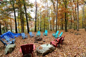A forest campsite with several Adirondack chairs arranged around a central fire pit. - Waterfront Cabin Ideal for Families and Outdoor Adventures in Arkansas (Fairfield Bay)