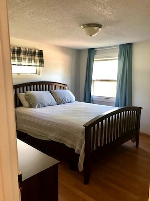 A bedroom with a wooden bed, a window with curtains, and a ceiling light.
