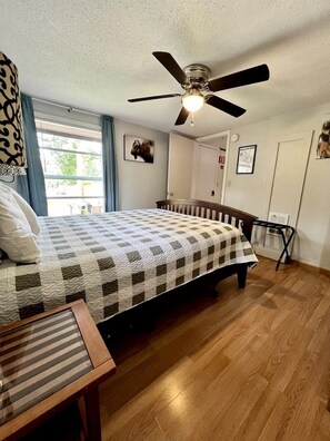 A bedroom with a bed, a ceiling fan, a window with curtains, and a door. - Buffalo Cabin #2 (Hot Springs)