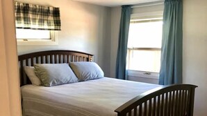 A bedroom with a wooden bed, a window with curtains, and a ceiling light.