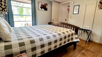 A bedroom with a bed, a ceiling fan, a window with curtains, a door, and a small table.
