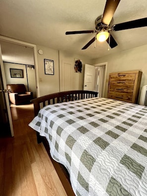 A bedroom with a bed, a ceiling fan, a wooden wardrobe, and a door leading to another room. - Buffalo Cabin #2 (Hot Springs)