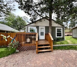 A small house with a wooden deck, a front door, and a window. - Unique Cabin with Deck Great for Families in South Dakota (Hot Springs)