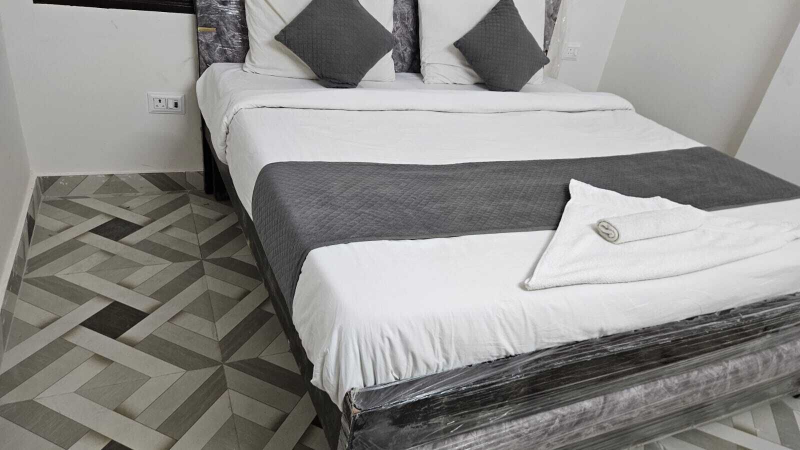 Una cama con colchón blanco y ropa de cama gris, incluye una manta gris y un almohadón con otro almohadón gris encima.
