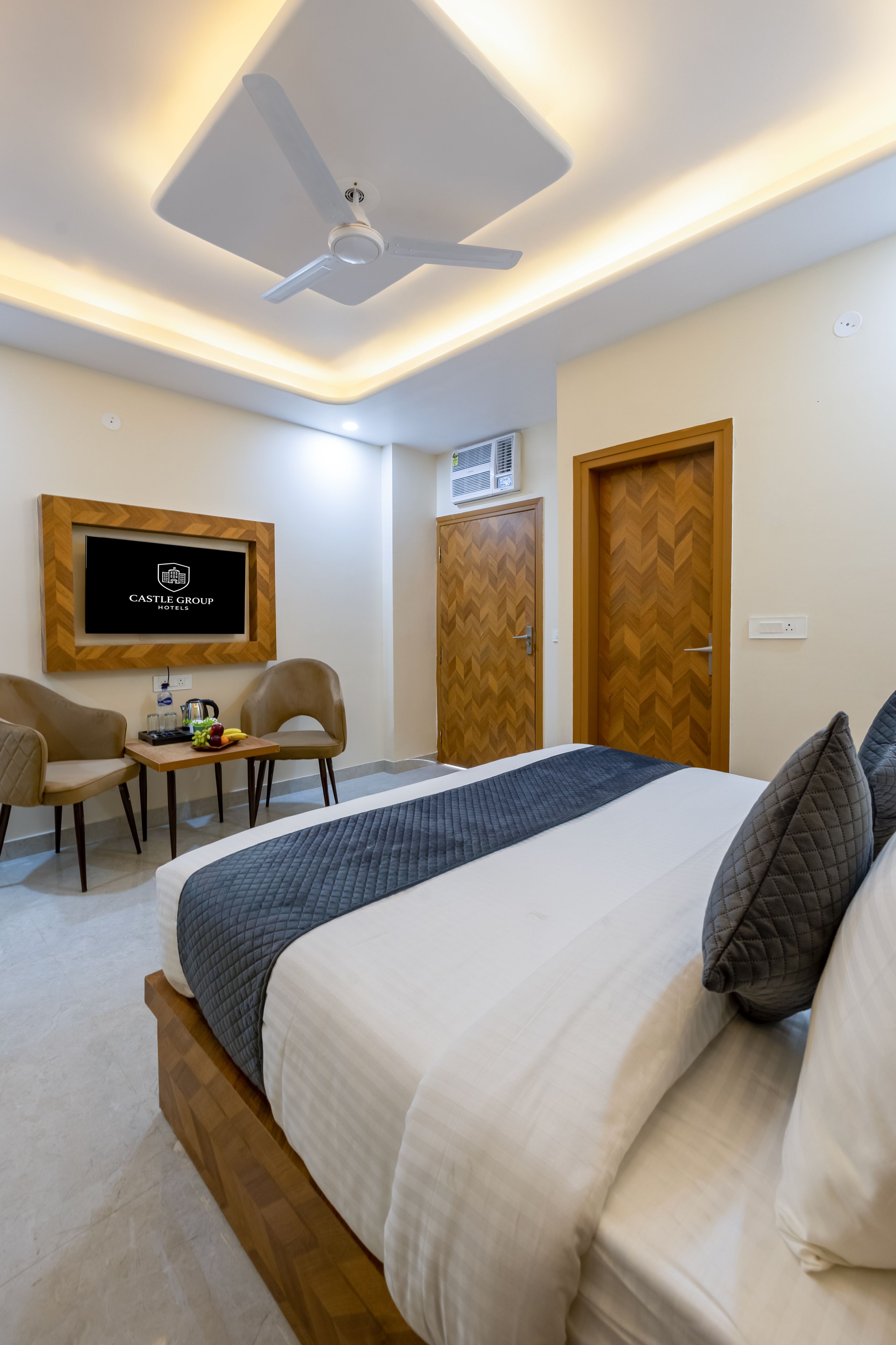 A hotel room with a bed, a desk with a chair, a television, and a ceiling fan.