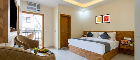 Quarto de hotel com cama, área de estar com uma cadeira, uma pequena mesa com petiscos e vista para o exterior.
