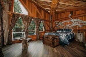 Ein rustikaler Raum mit Holzboden, einem Bett, einem Koffer und einem großen Fenster.