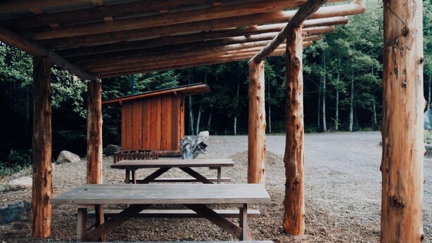 Uma estrutura de madeira rústica com uma mesa de piquenique e um pequeno edifício semelhante a uma cabana.