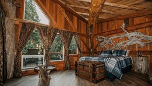 Um quarto rústico de madeira com uma cama, um baú e uma grande janela.