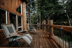 A wooden deck with outdoor seating and a view of a forest. - Off-Grid Log Cabin near Olympic National Park, Perfect for a Weekend of Hiking in Temperate Rainforests (Forks)