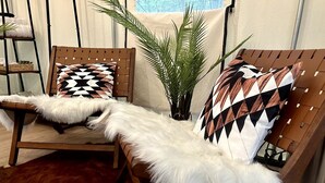 Un área de descanso con dos sillones de madera, uno con un plaid blanco y suave, y el otro con un cojín estampado. Una planta grande en maceta se encuentra en el centro.