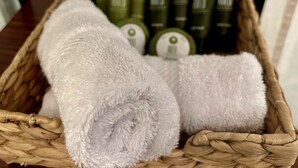 Una cesta tejida con toallas enrolladas y botellas verdes.