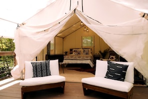 A tented accommodation with a bed, two cushioned seating areas, and a wooden deck.