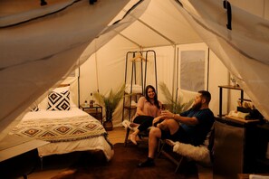 A tented accommodation with a bed, a chair, a small table, and a hanging chair.