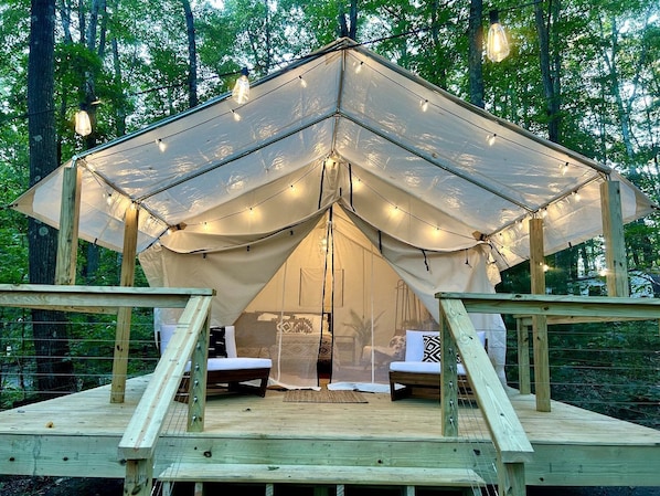 A tented accommodation with a wooden deck, two seating areas, and string lights.