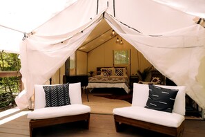 A tented accommodation with a bed, two cushioned seating areas, and a view of the outdoors.