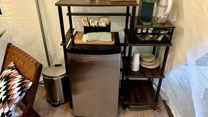 Una kitchenette compacta con refrigerador, cafetera y pequeño comedor con una silla y mesa.