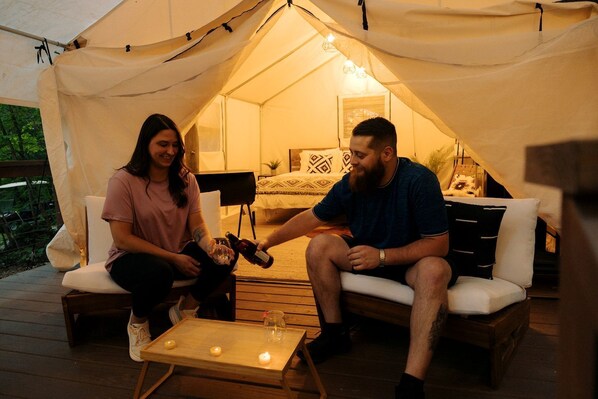 A tented accommodation with a wooden deck, a small table with candles, and a bed with patterned bedding.