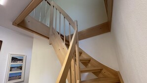 A wooden staircase with a handrail, white walls, and a framed picture of a coastal scene. - Vacation home "MeerZeit" - Holiday home over 3 floors, 65 m² living space with terrace (Dahme)