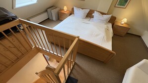 A bedroom with a wooden bed, two bedside tables with lamps, a window, and a small stool. - Vacation home "MeerZeit" - Holiday home over 3 floors, 65 m² living space with terrace (Dahme)