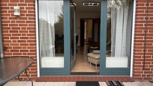 A modern building with a brick facade, a glass door entrance, and a visible living room area with a sofa and a coffee table. - Vacation home "MeerZeit" - Holiday home over 3 floors, 65 m² living space with terrace (Dahme)