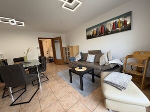 A modern living room with a sofa, coffee table, and a dining area with chairs and a table. - Vacation home "MeerZeit" - Holiday home over 3 floors, 65 m² living space with terrace (Dahme)