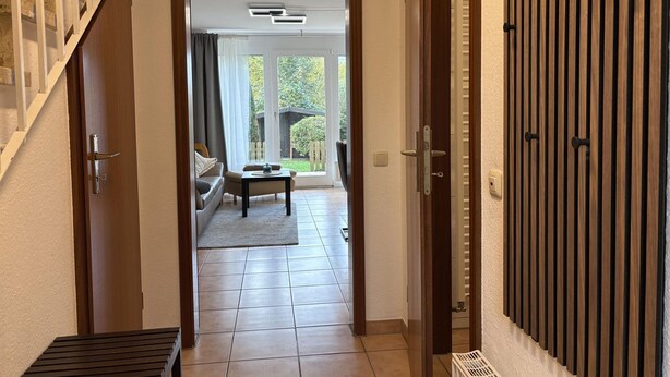 A hallway with a staircase on the left, a door on the right, and a view into a living area with a sofa, table, and large windows. - Vacation home "MeerZeit" - Holiday home over 3 floors, 65 m² living space with terrace (Dahme)