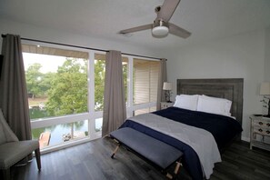 Ein Schlafzimmer mit Bett, einer Bank, einem Sessel, einem Nachttisch, einer Lampe und einem Deckenventilator.
