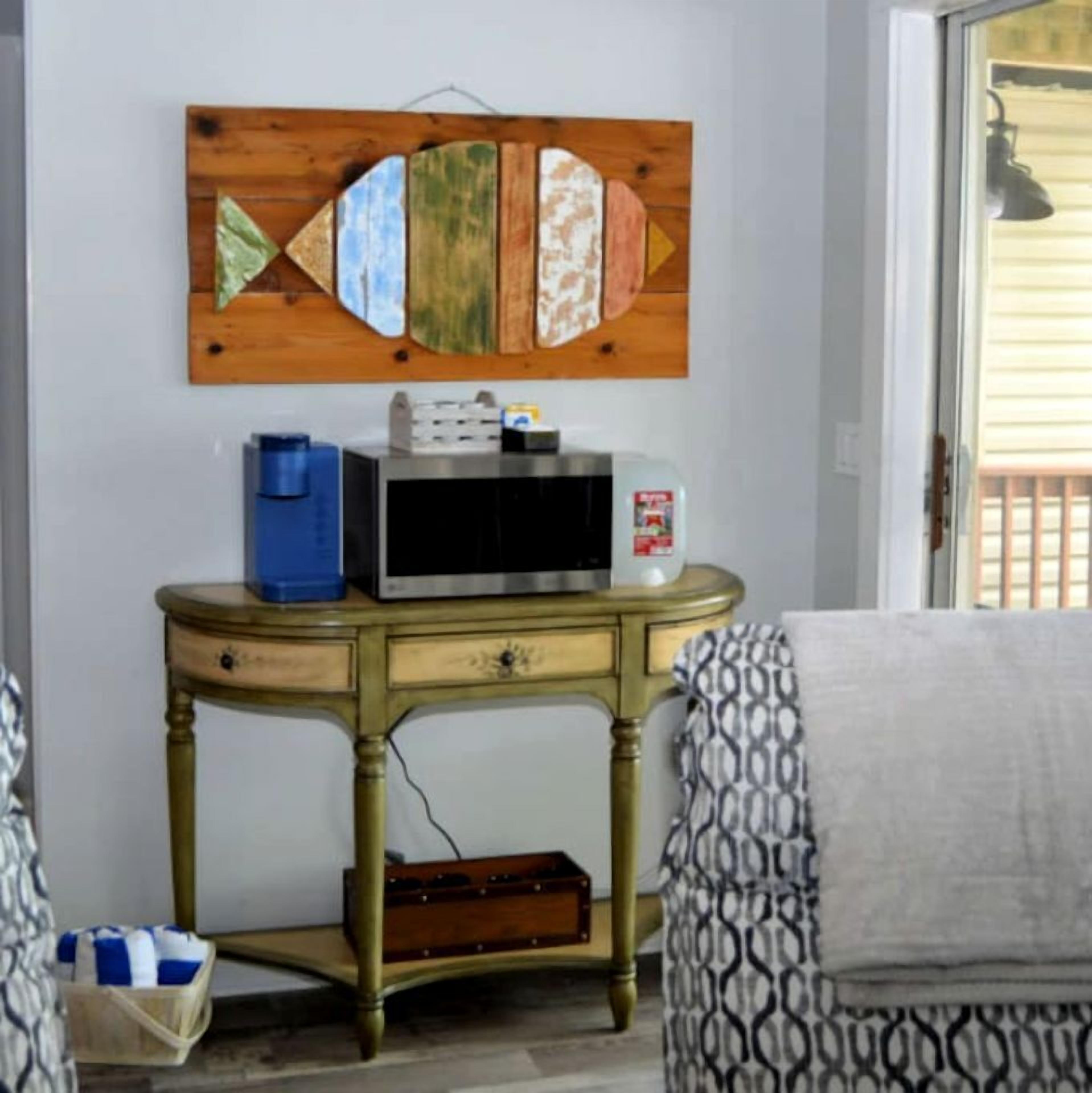 A room with a wooden wall art piece, a small table with a microwave, and a patterned chair.
