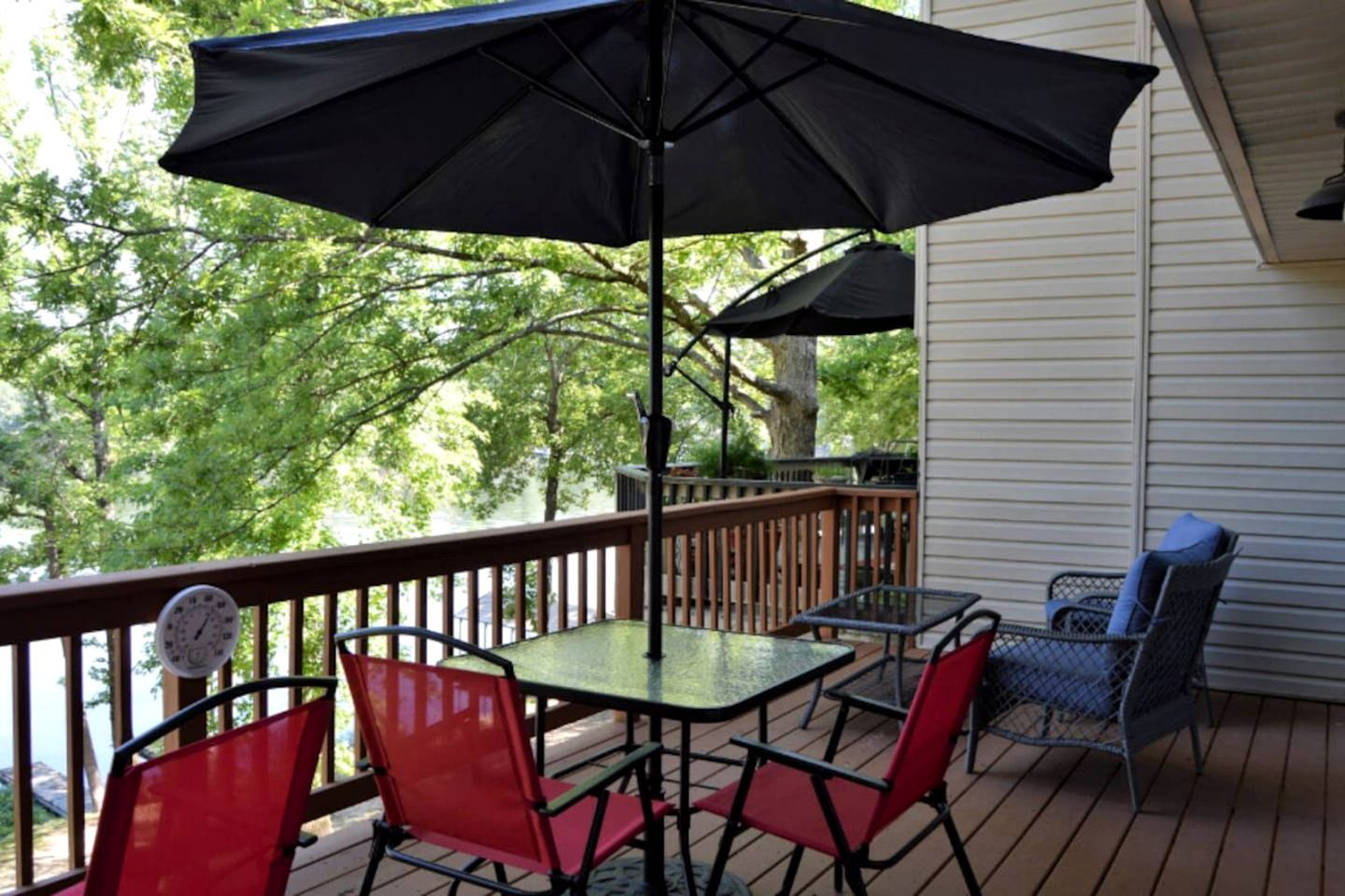 A covered outdoor deck with a table and chairs, a railing, and a view of trees.