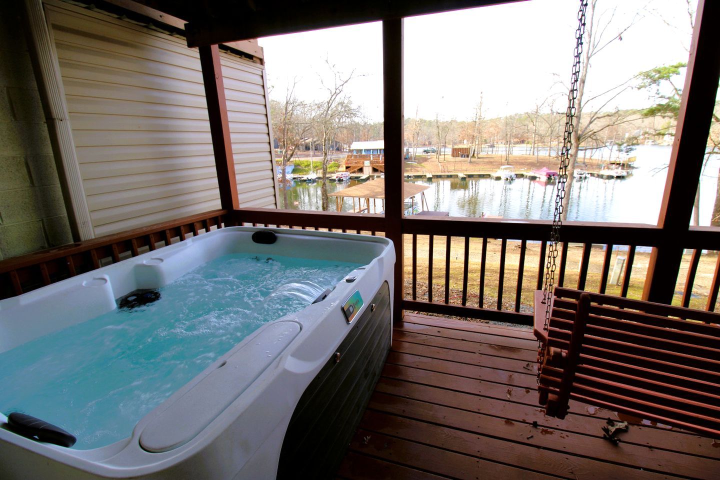 A hot tub on a wooden deck with a view of a lake and boats.